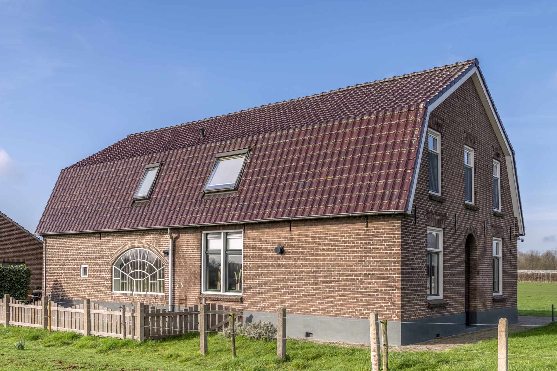 Aanzicht van een verbouwde bakstenen boerderij in Afferden met een maatwerk wit stalen korfboograam in de achtergevel