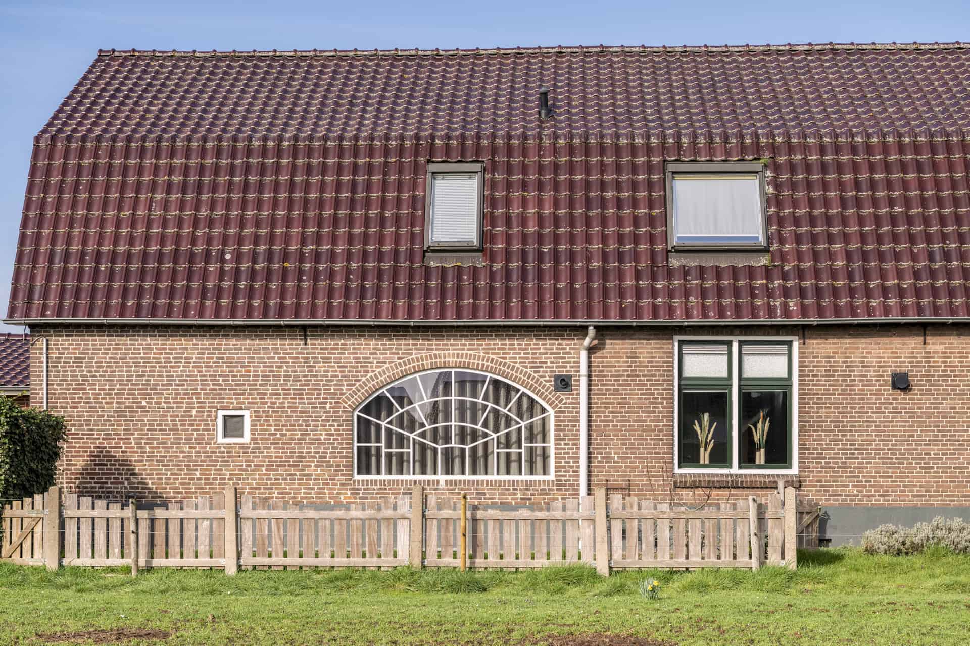 Achtergevel van een boerderij met een groot wit stalen korfboograam en een aangrenzend rechthoekig stalraam