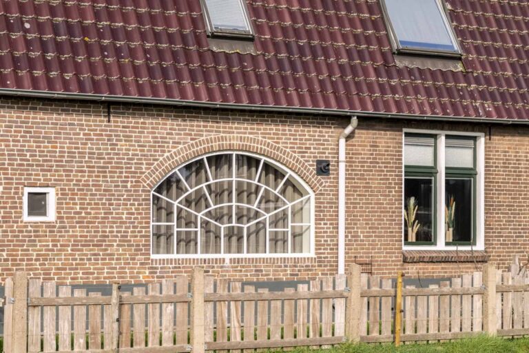 Detailaanzicht van het witte stalen korfboograam in de bakstenen gevel met zichtbare roedenverdeling